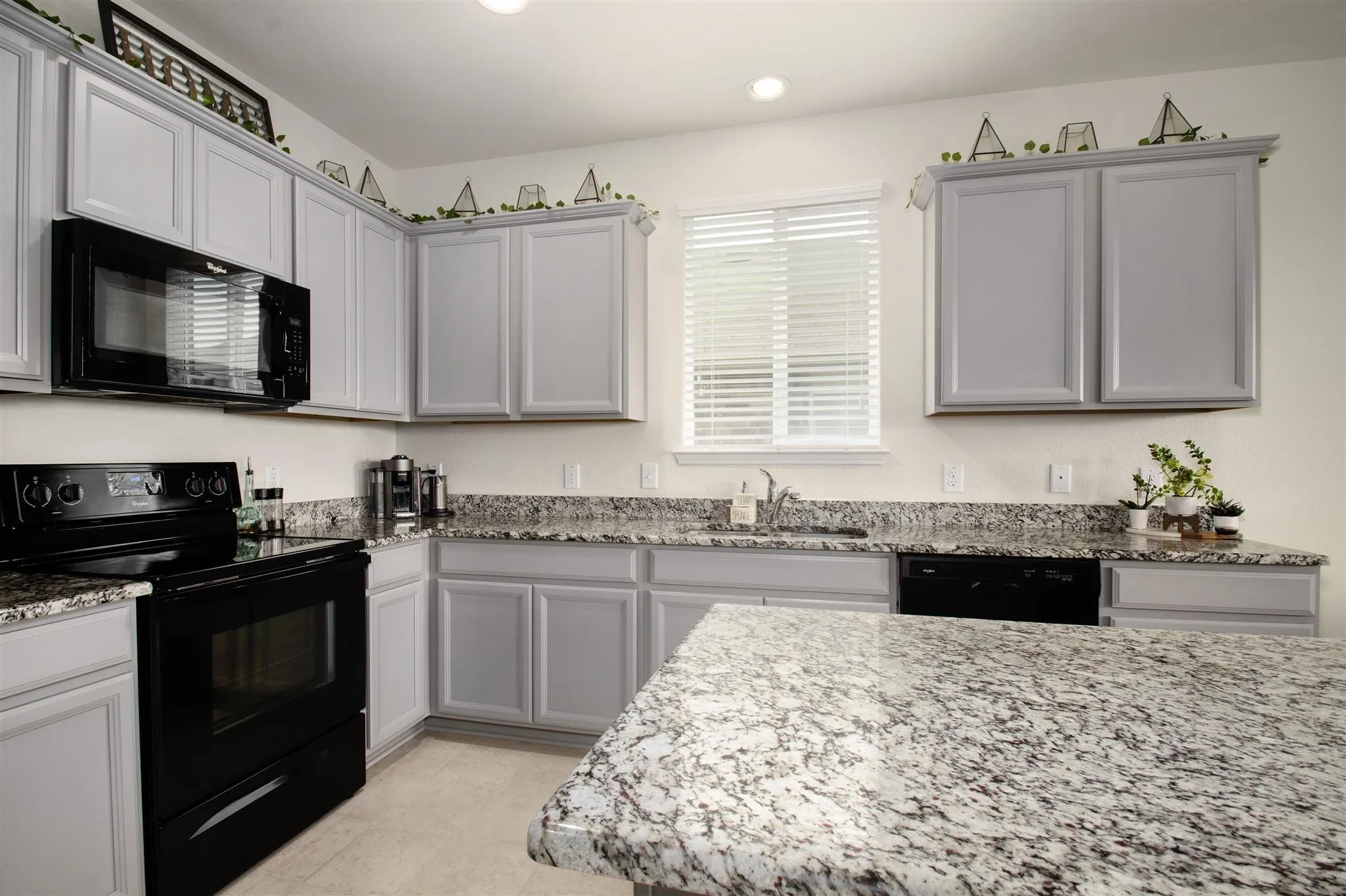 Kitchen featuring light gray cabinetry, granite-style countertops, stainless steel sink, and black appliances