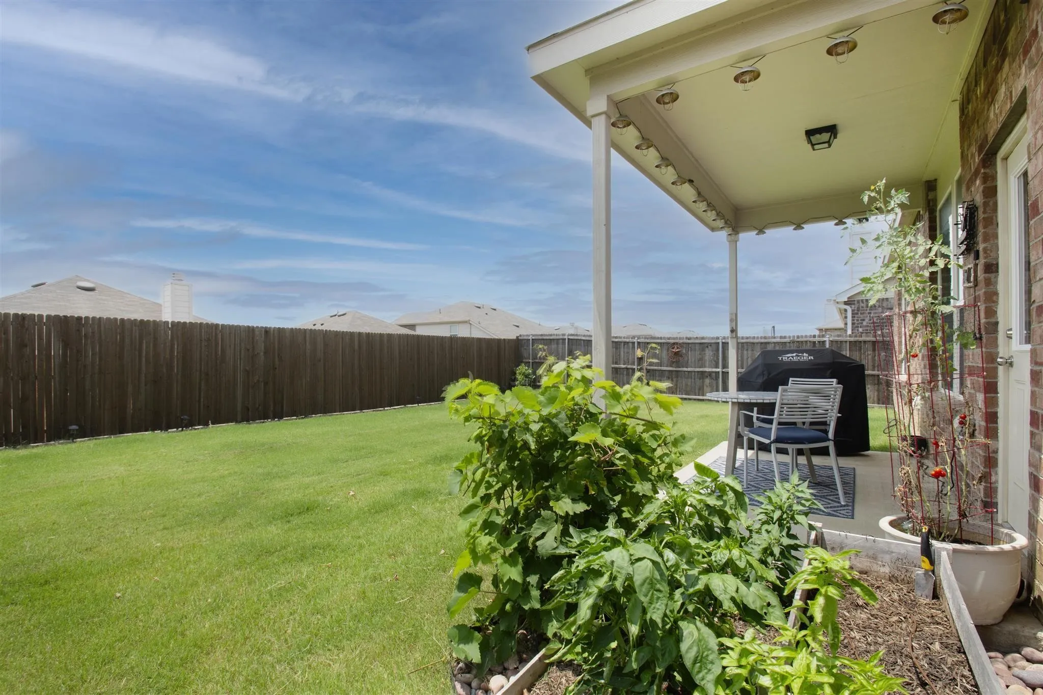 Expansive grassy yard with a wood privacy fence, featuring a covered patio, brick exterior, and recessed lighting