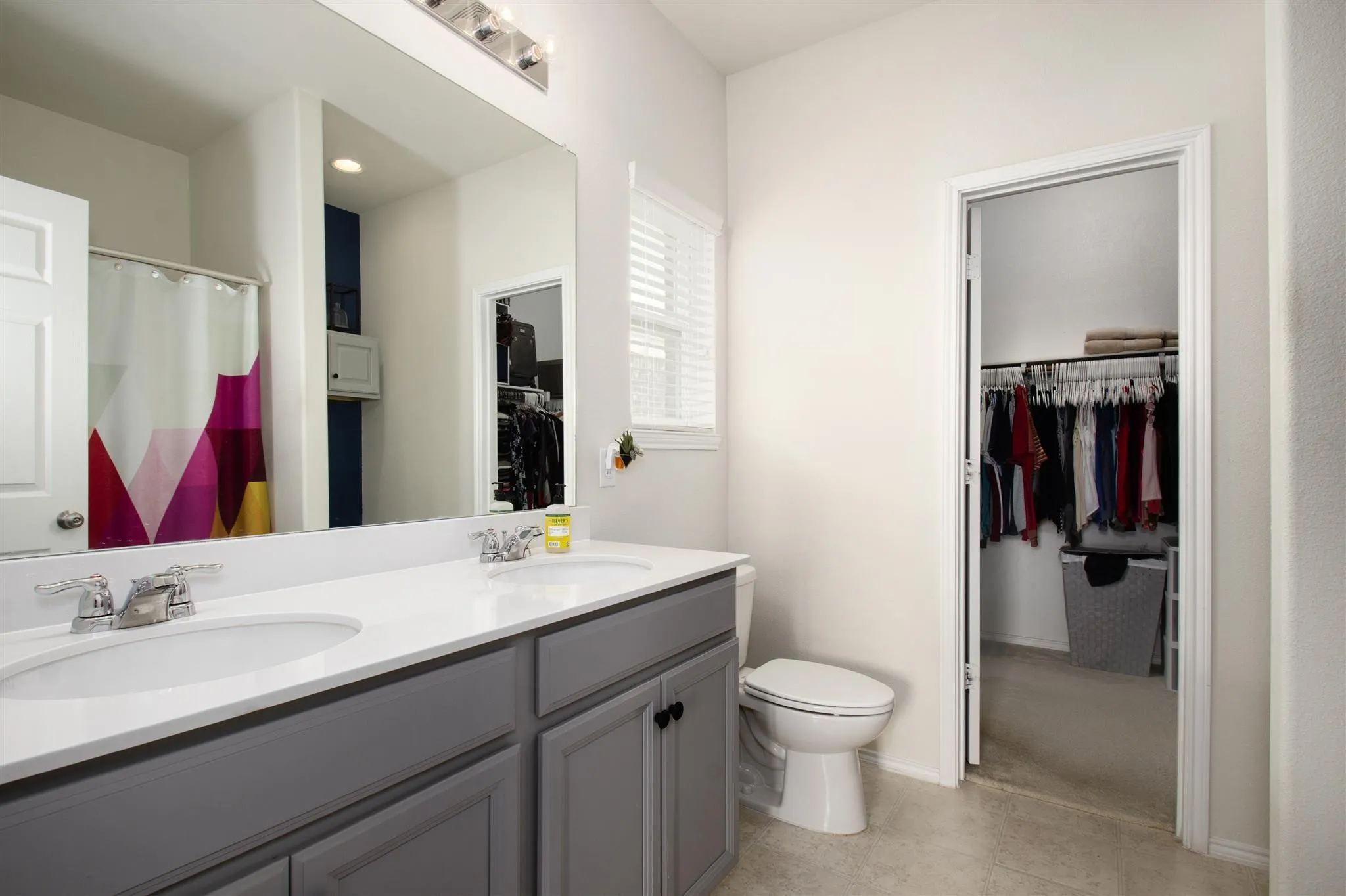 Dual sink vanity with a white countertop and gray cabinetry, elongated toilet, and built-in closet storage