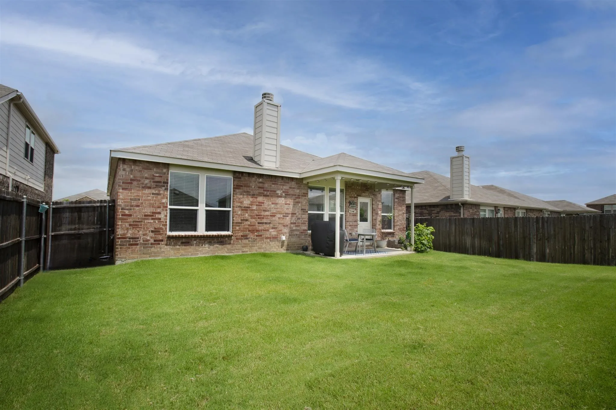 Expansive green lawn with a covered patio, brick exterior, and a privacy fence