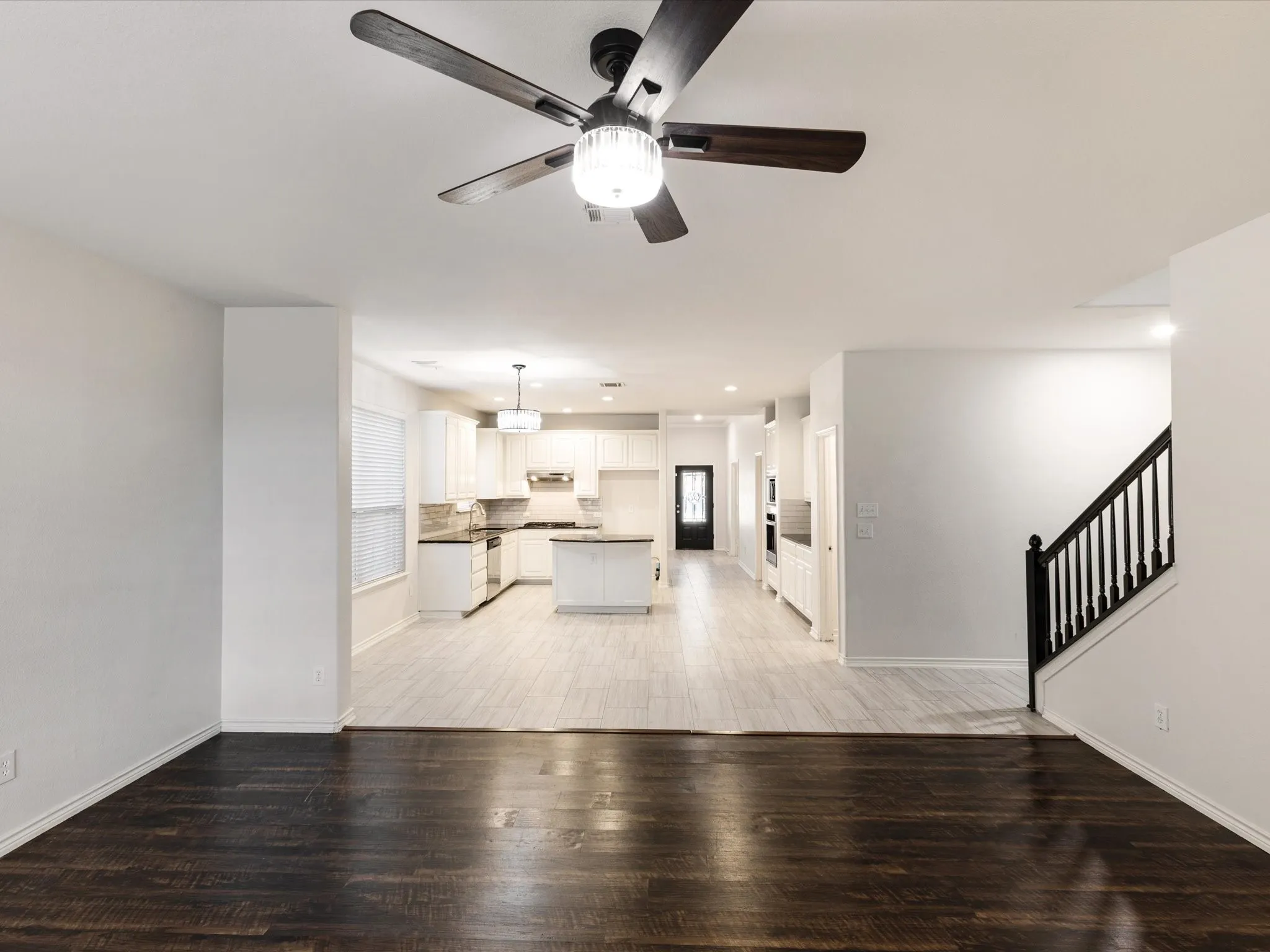 Open-concept living space featuring wood-finish flooring, a contemporary ceiling fan, and a kitchen with white cabinetry, dark countertops, and an island