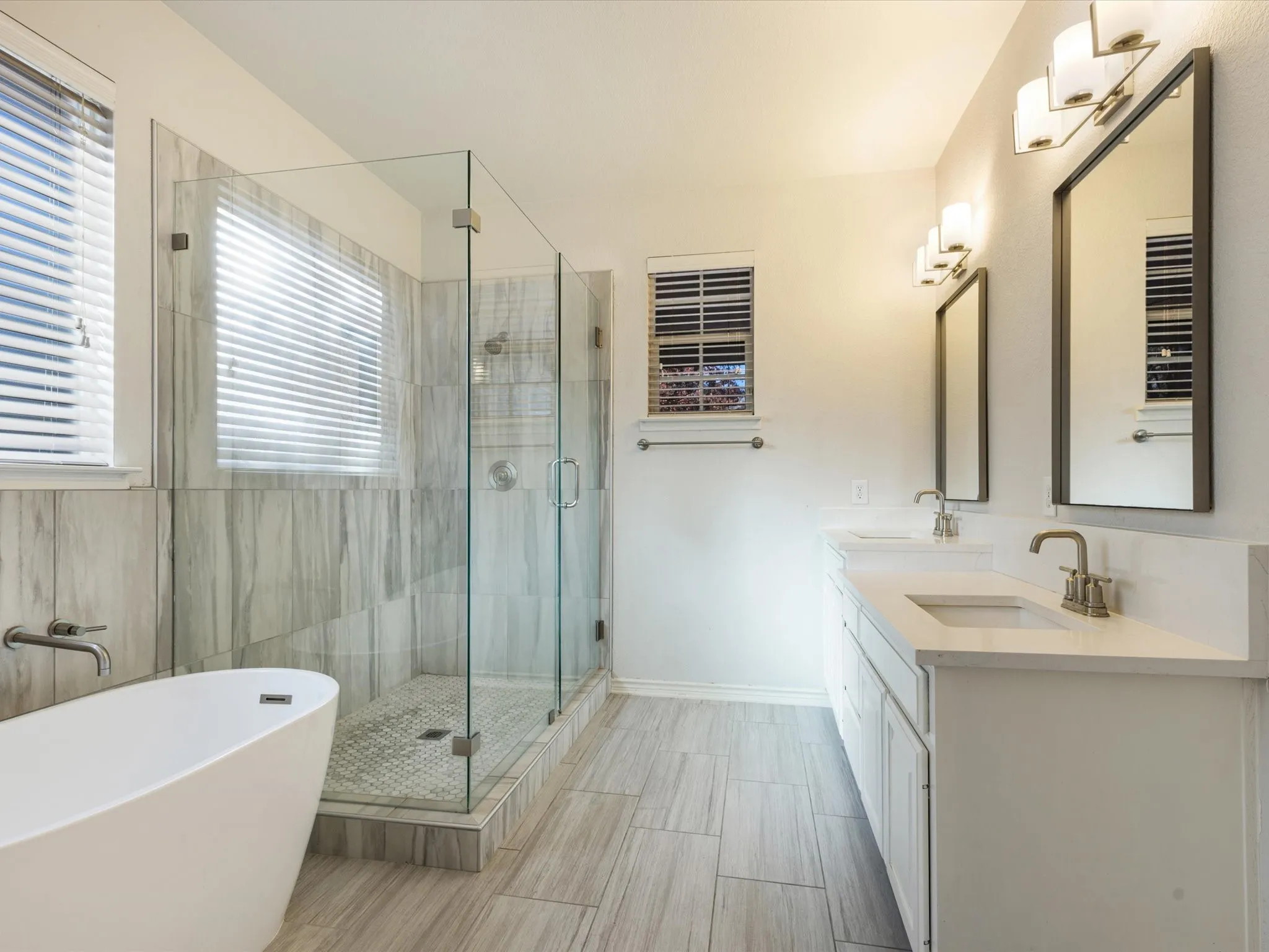 Freestanding soaking tub, glass-enclosed shower, dual vanities with undermount sinks, and plank-style tile flooring
