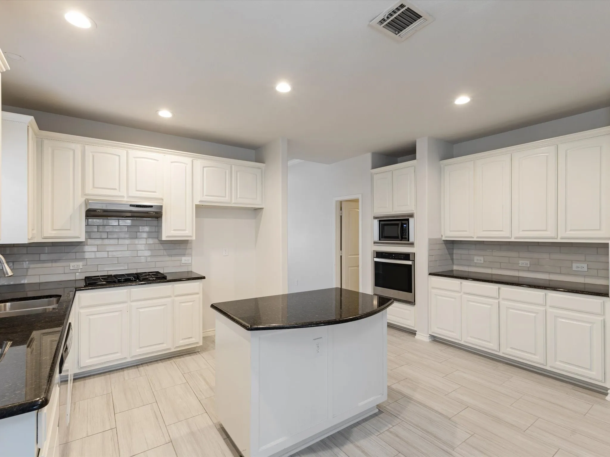 Bright kitchen featuring white cabinetry, dark countertops, subway tile backsplash, and light wood-finish flooring