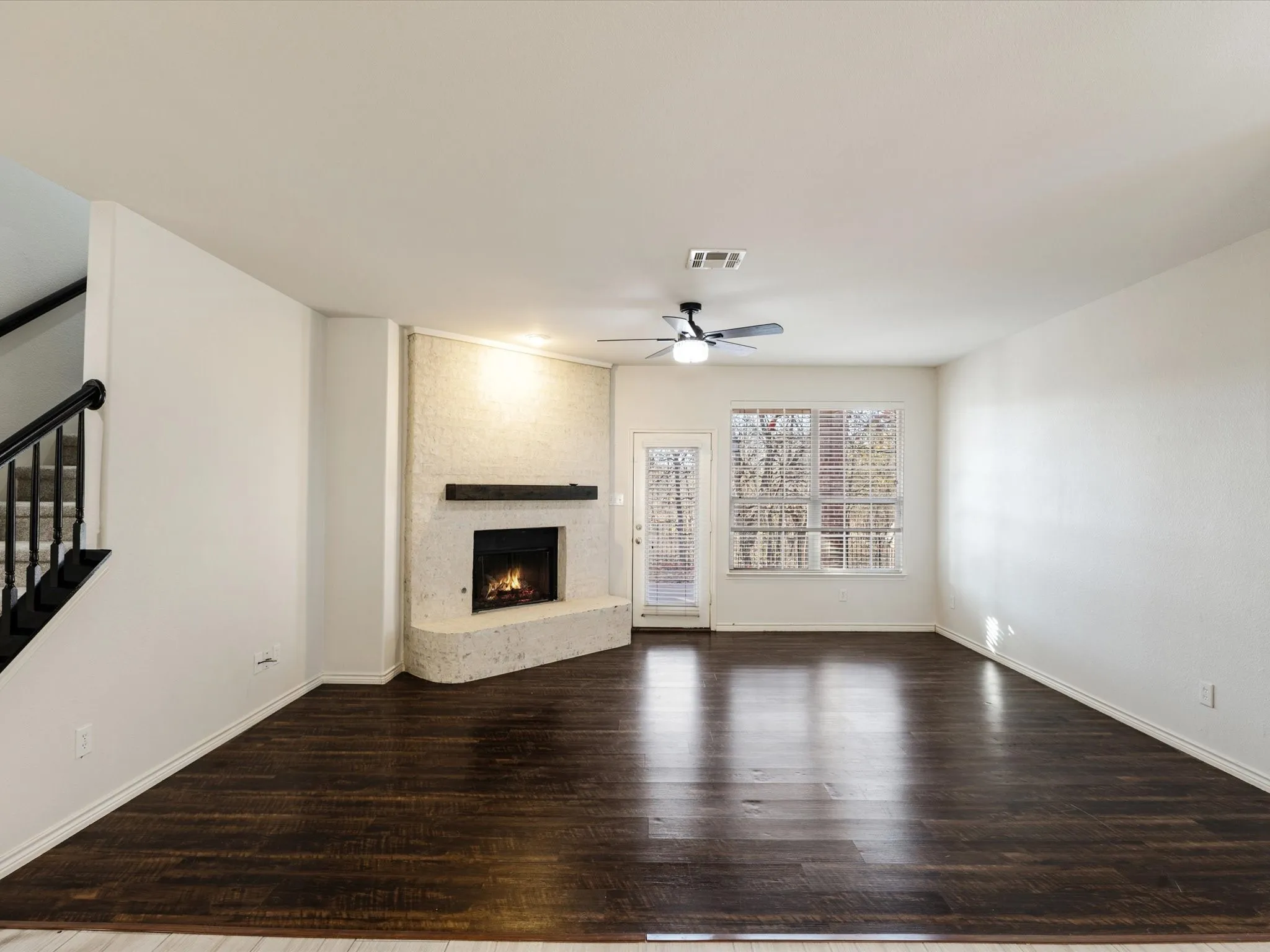 Expansive room featuring wood-finish flooring, a corner fireplace with a mantel, and a ceiling fan