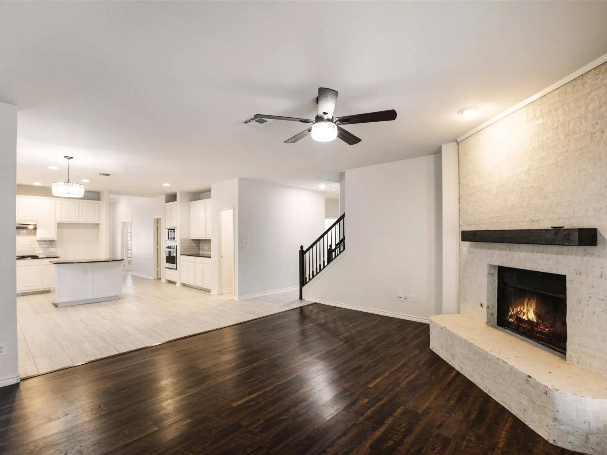 Stone-clad fireplace with a wood mantel, dark wood-finish flooring, white cabinetry, integrated stainless steel appliances, and a central island