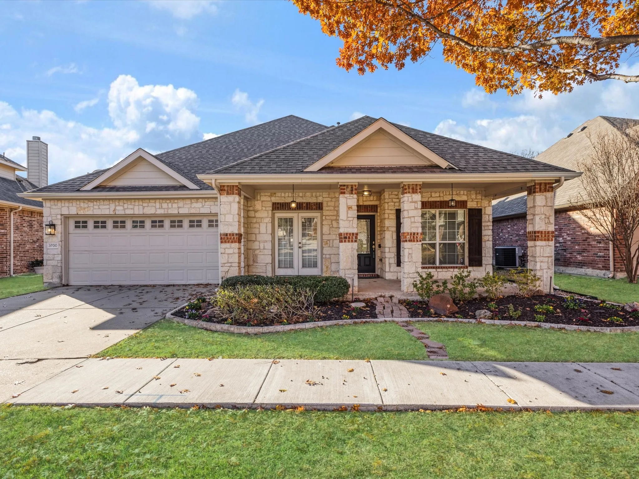 Stone and brick exterior with a covered porch, an attached two-car garage, and a manicured front lawn
