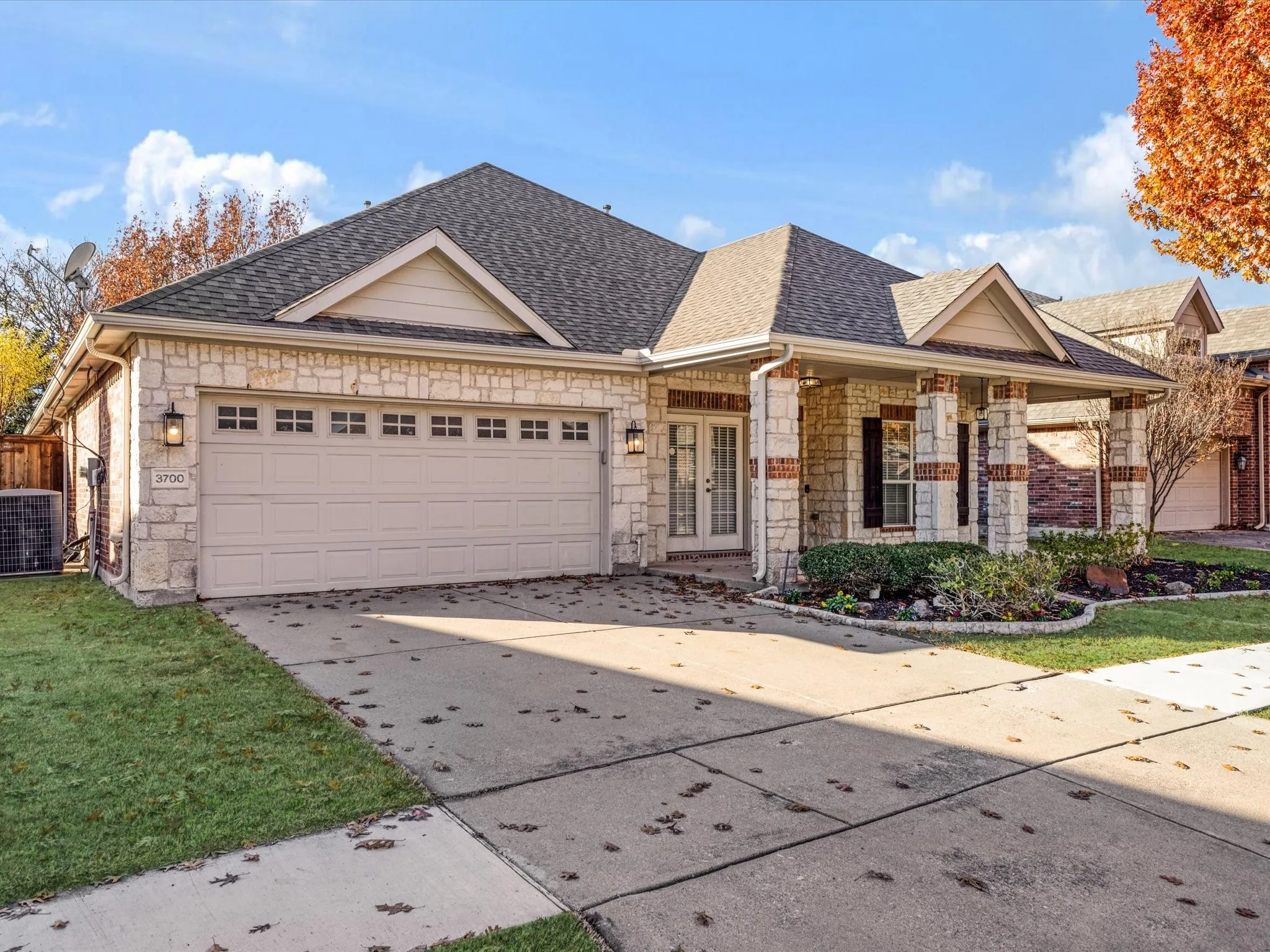 Stone and brick exterior with a covered porch, a two-car garage, and a concrete driveway