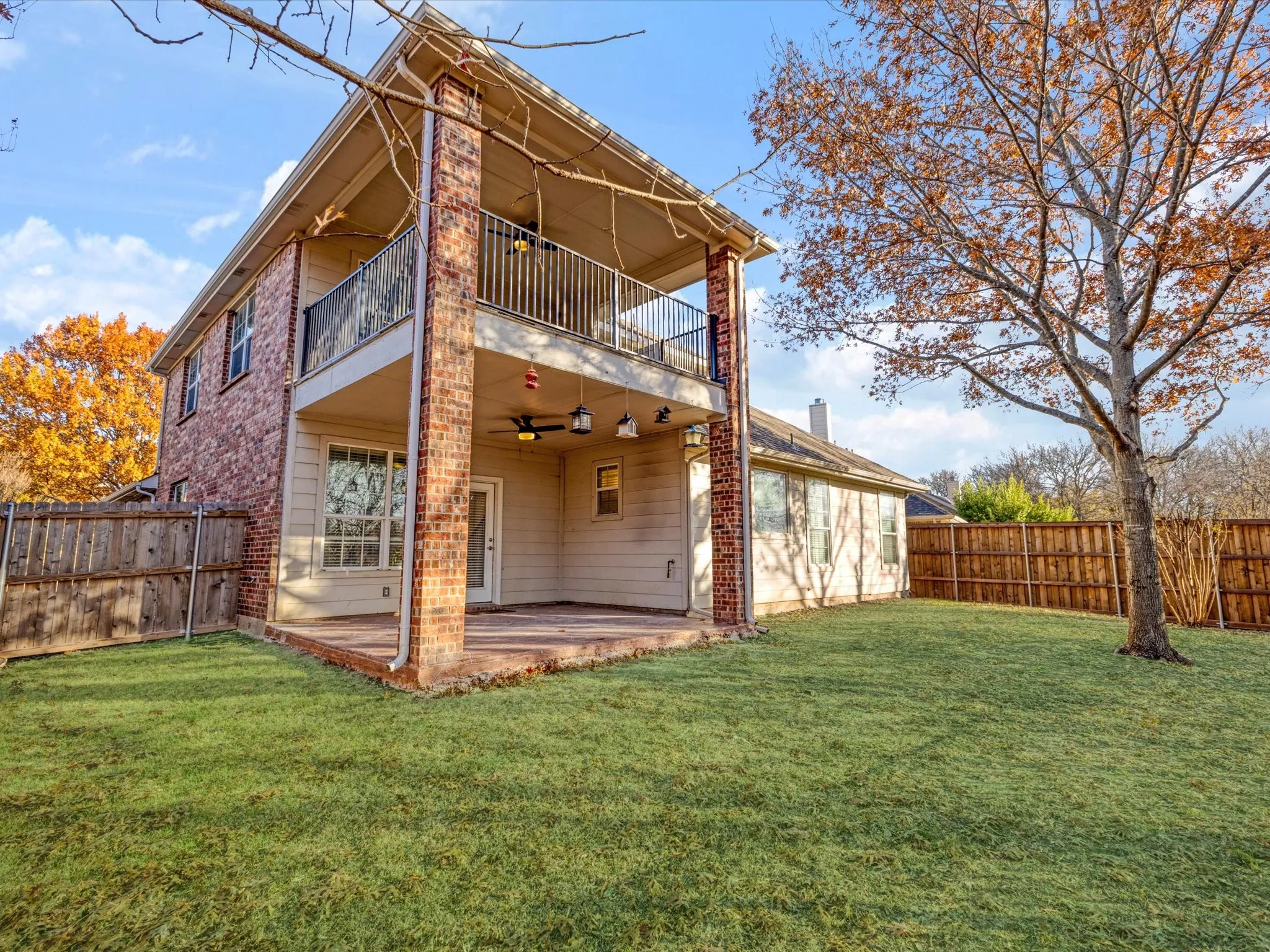 Two-story exterior with brick and siding, featuring a covered patio, second-story balcony with metal railing, and a fenced yard