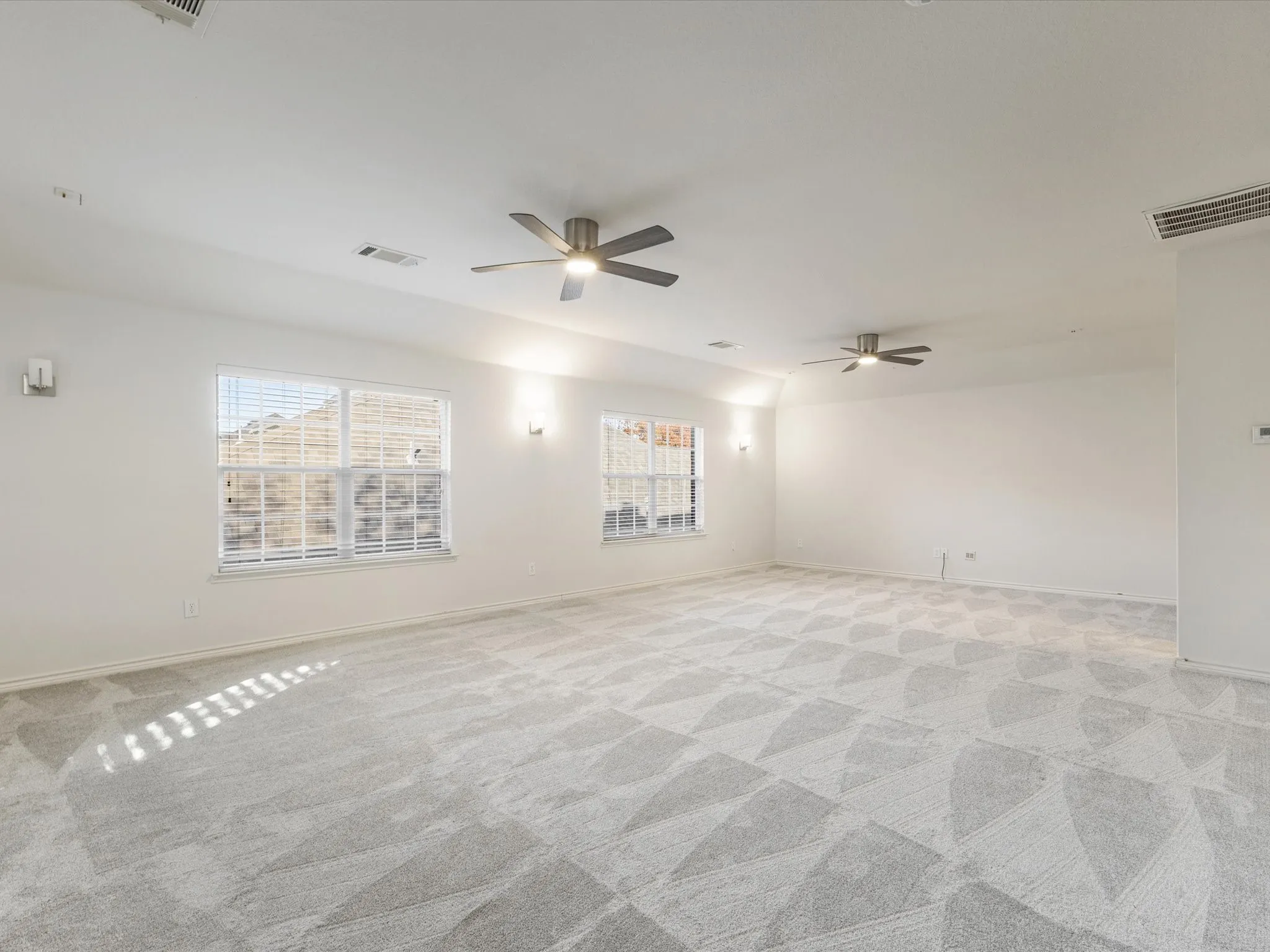 Expansive room featuring light-colored patterned carpeting, multiple windows, two ceiling fans, and wall sconces