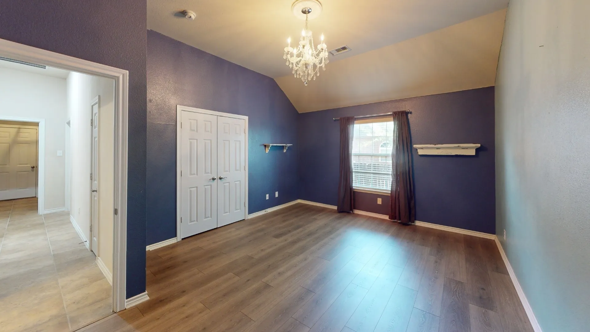 Vaulted ceiling, wood-finish flooring, white double-door closet, decorative wall sconce, and chandelier