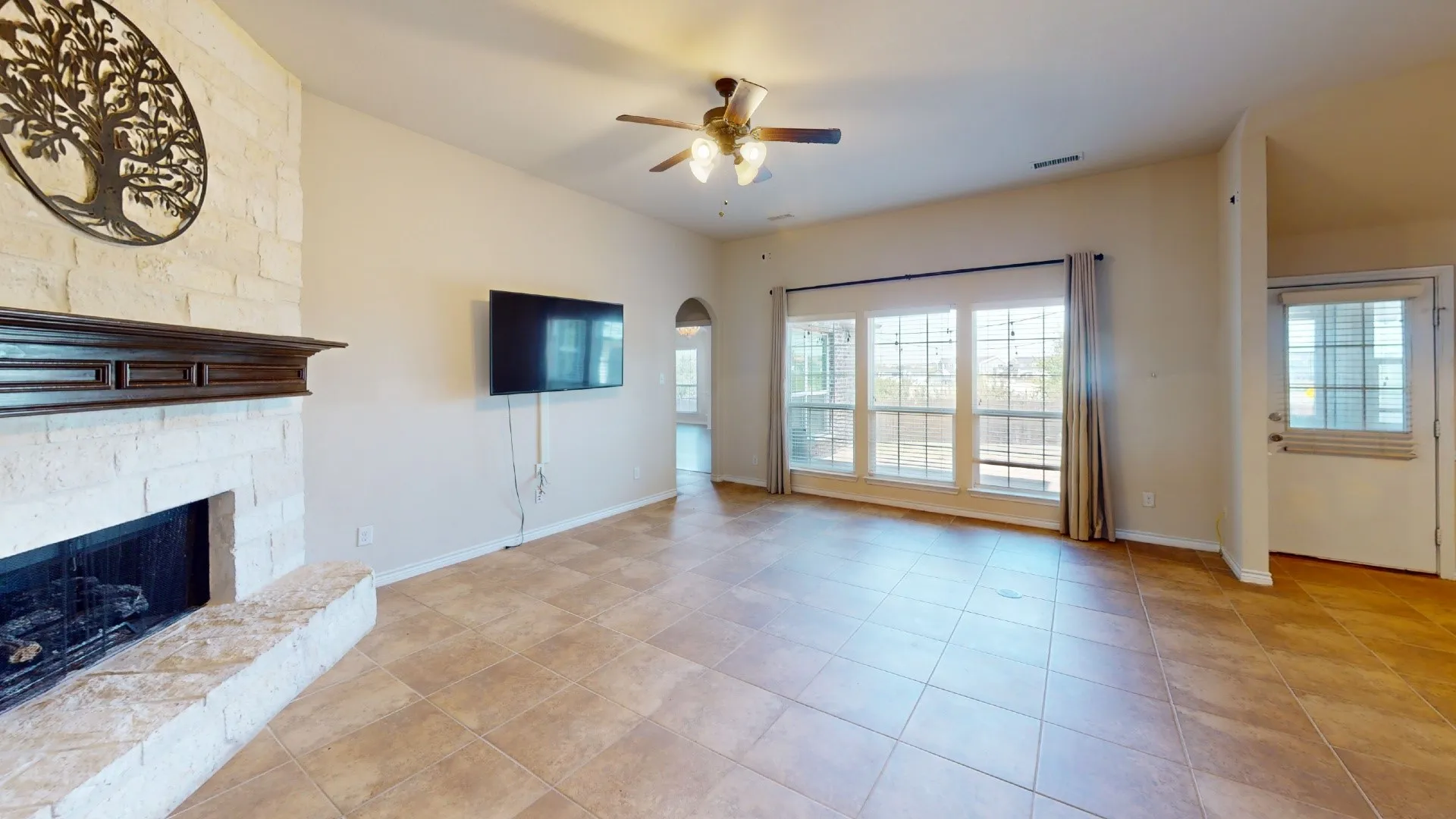 Stone-clad fireplace with dark wood mantel, vaulted ceilings, tiled flooring, multi-paned windows, and a ceiling fan with integrated lighting