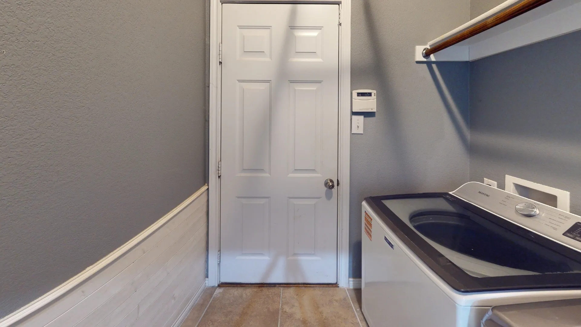 Tile flooring, white paneled door, gray wall finish, white wainscoting, and an integrated clothing rod