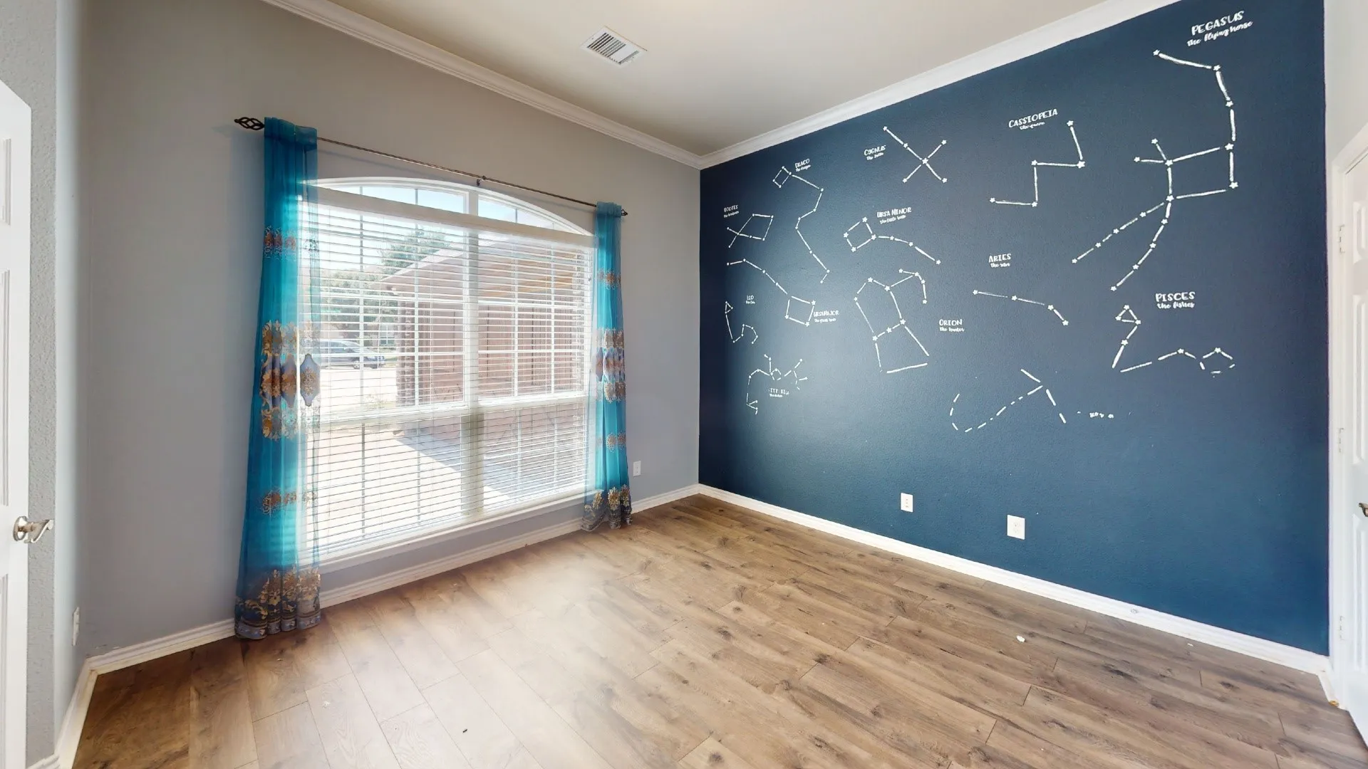 Bright, naturally lit bedroom featuring hardwood flooring, neutral wall finishes, and an accent wall with celestial constellation design