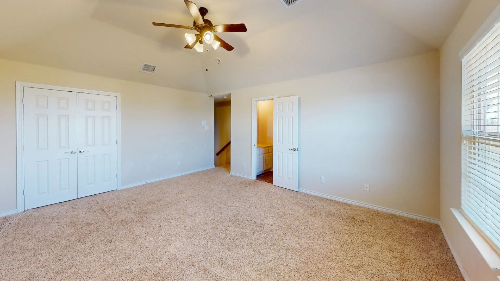 Expansive room featuring vaulted ceilings, neutral carpeting, and a ceiling fan with integrated lighting