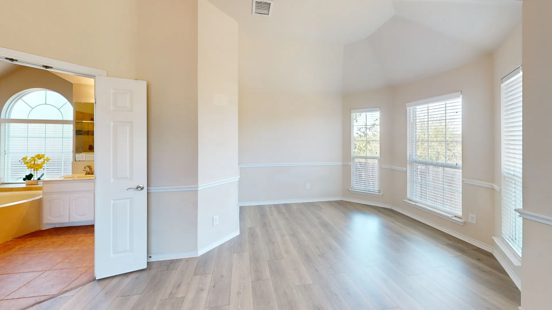 Vaulted ceiling, wood-finish flooring, architectural molding, multiple windows, and an arched window in the adjacent room