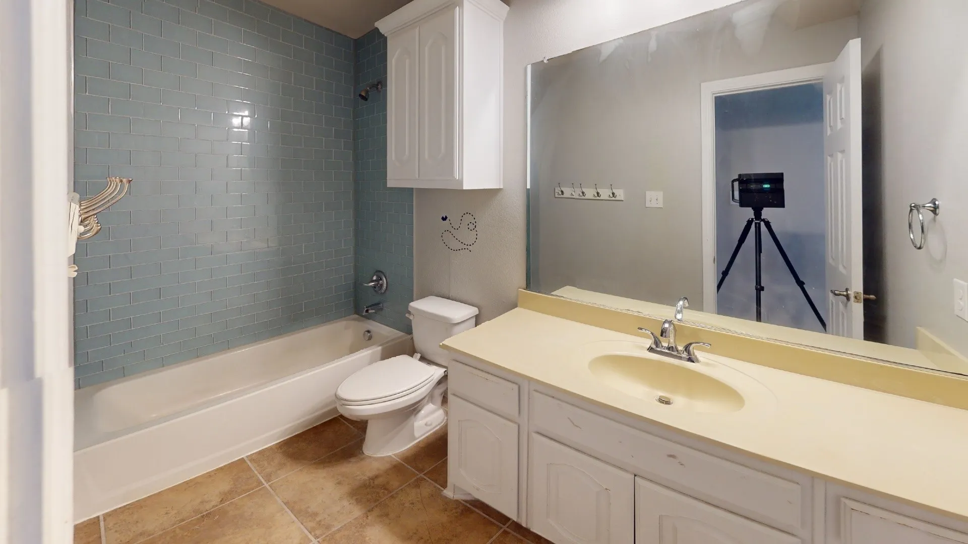 Bathtub with blue subway tile surround, single vanity with integrated sink, white cabinetry, wall-mounted mirror, and tile flooring