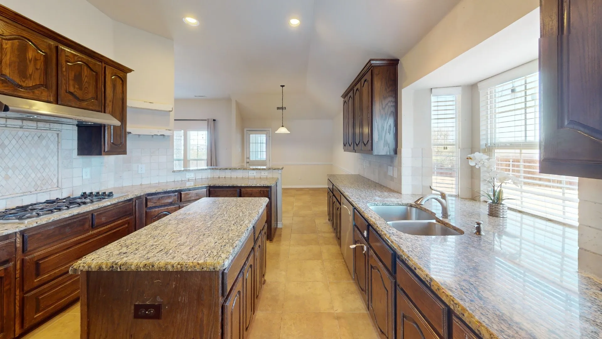 Kitchen featuring granite countertops, wood cabinetry, tile backsplash, stainless steel appliances, and a central island