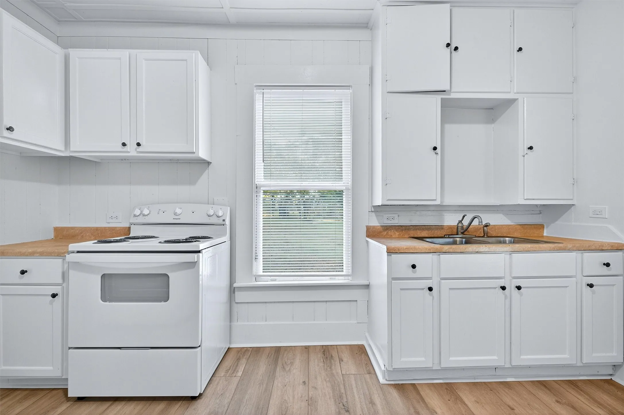 Kitchen featuring white cabinets, electric range, light countertops, light wood-style floors, and wooden walls