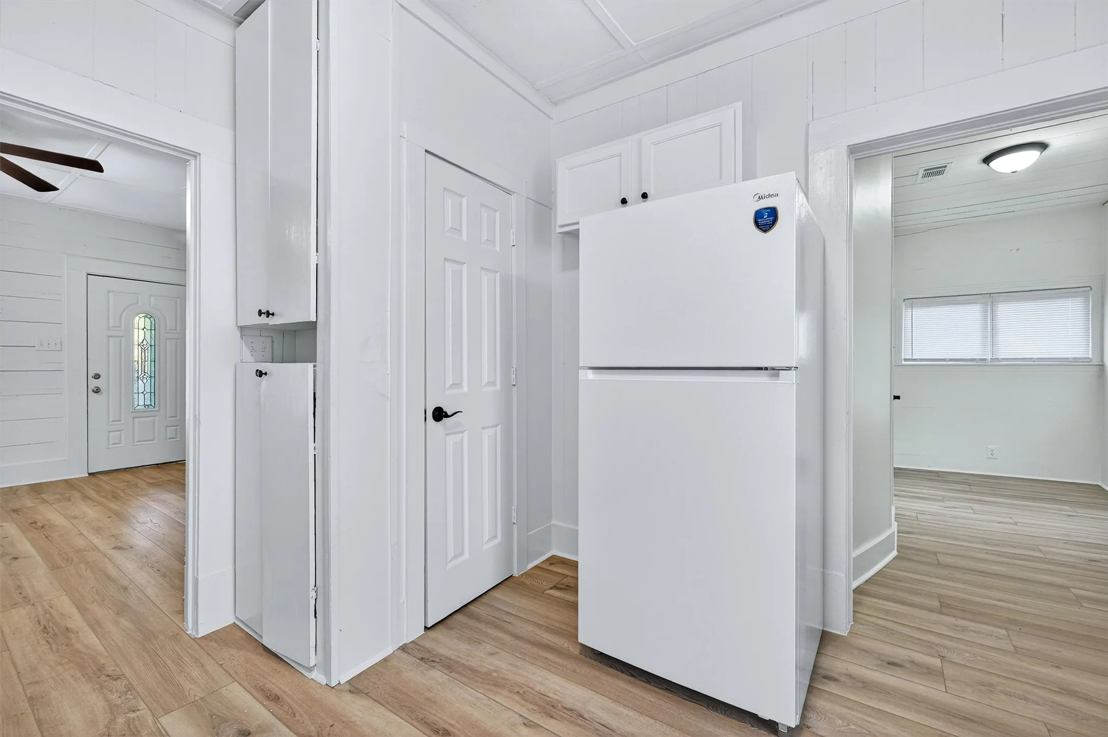 Kitchen featuring freestanding refrigerator, plenty of natural light, light wood-type flooring, white cabinets, and wooden walls