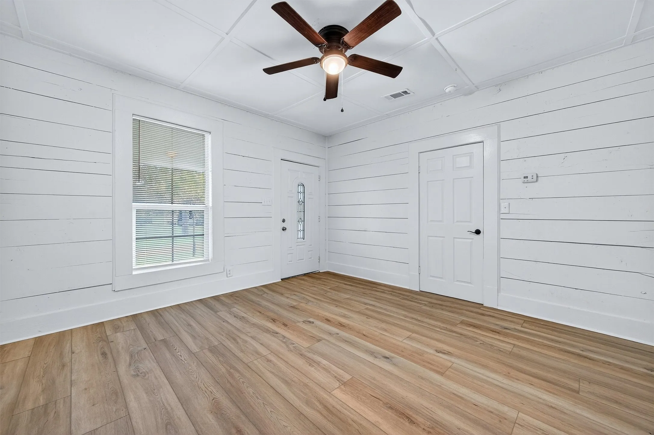 Empty room featuring light wood-type flooring, wood walls, and ceiling fan