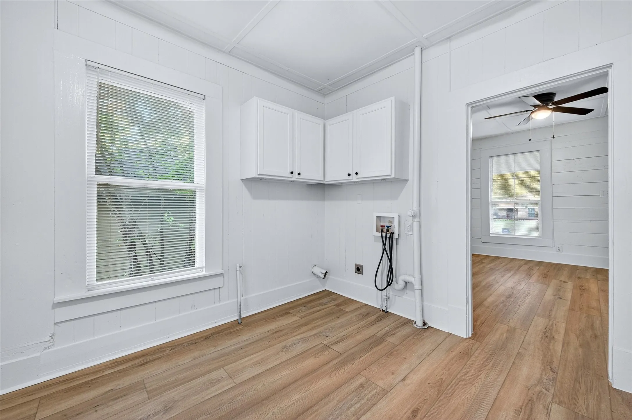 Laundry area with light wood-style flooring, washer hookup, cabinet space, wood walls, and a ceiling fan