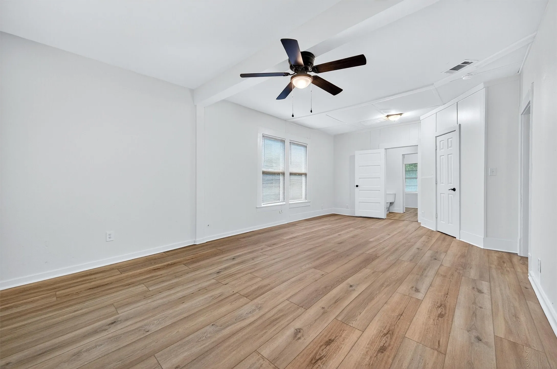 Unfurnished bedroom with light wood finished floors, a ceiling fan, and beamed ceiling