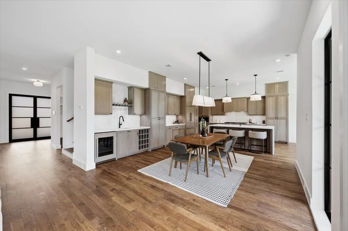 Open-concept living area with wood-finish flooring, a contemporary kitchen island, a built-in wet bar, and sleek pendant lighting