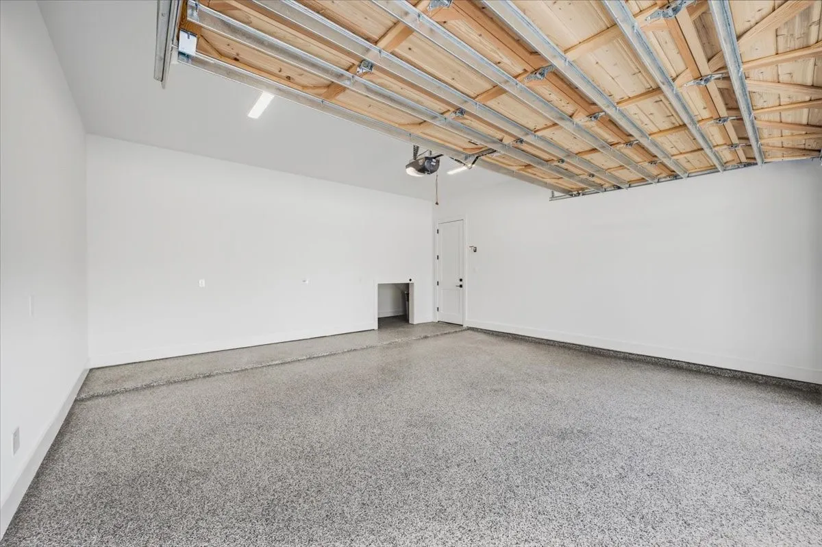 Spacious garage featuring a durable epoxy floor coating, white painted walls, and exposed ceiling joists