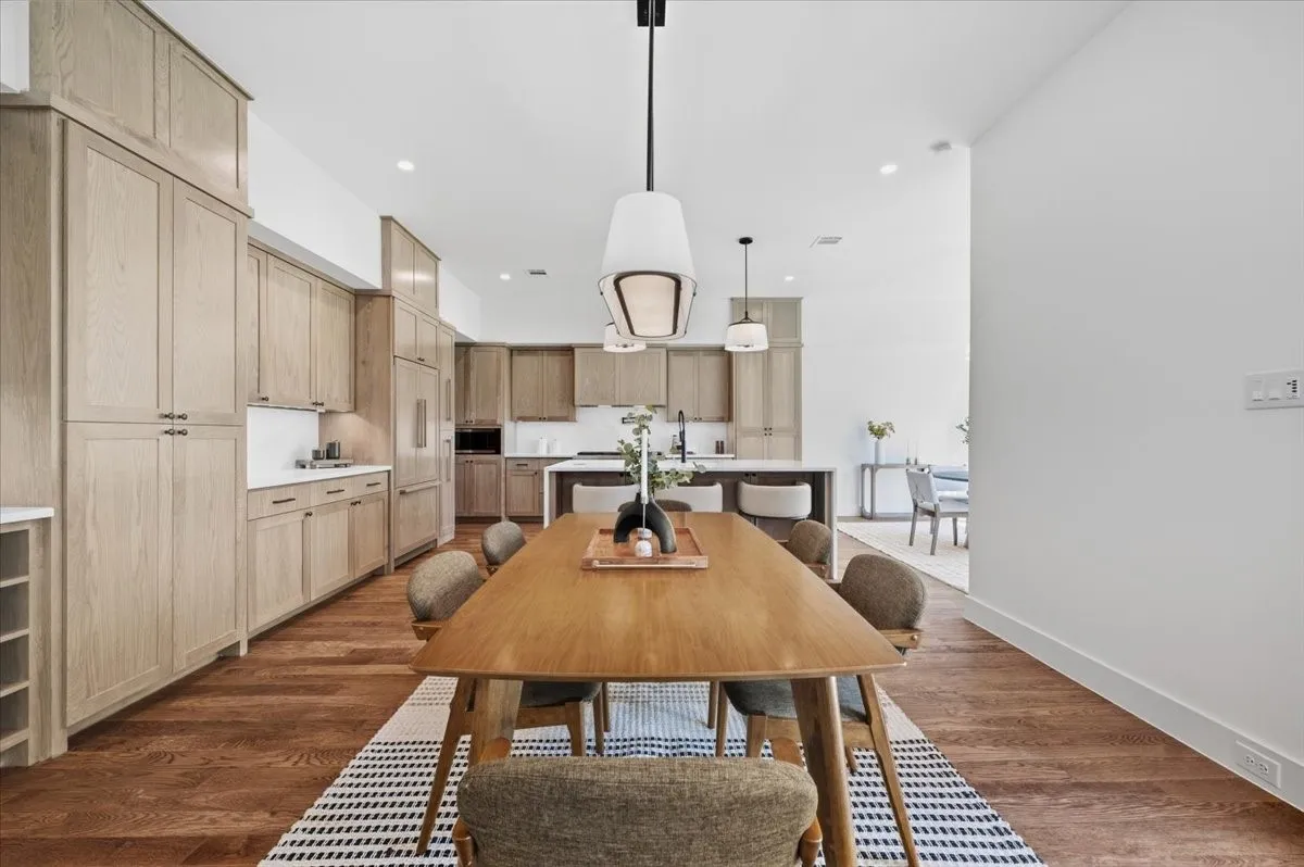 Wood-finish flooring throughout, modern pendant lighting, white walls, and extensive light wood-finish cabinetry