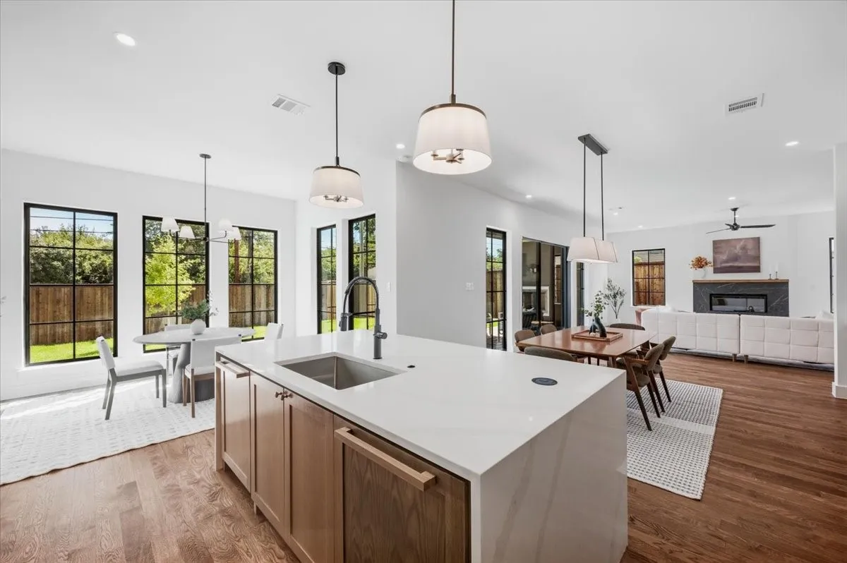 Kitchen island with a waterfall countertop and integrated sink, pendant lighting, wood-finish flooring, and a contemporary fireplace