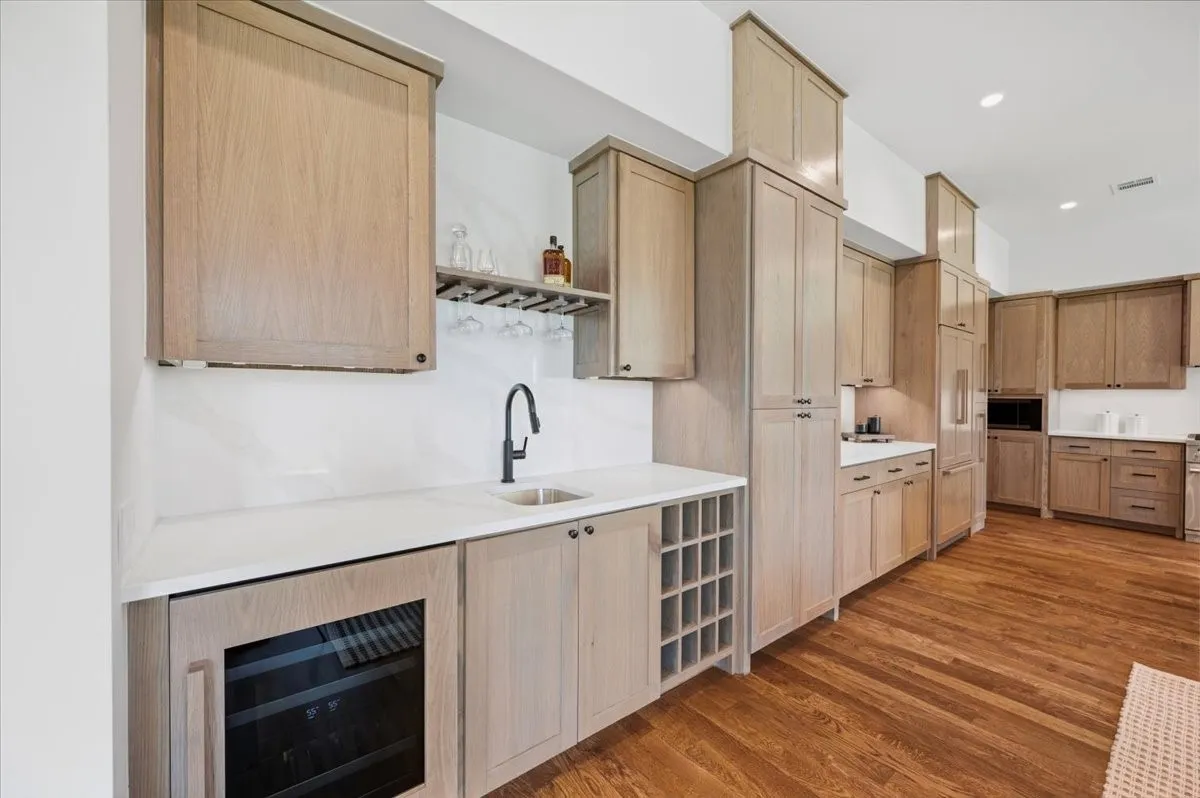 Hardwood flooring throughout, full-height light wood-finish cabinetry, integrated wine cooler, built-in wine rack, and a dedicated beverage sink with a matte black faucet