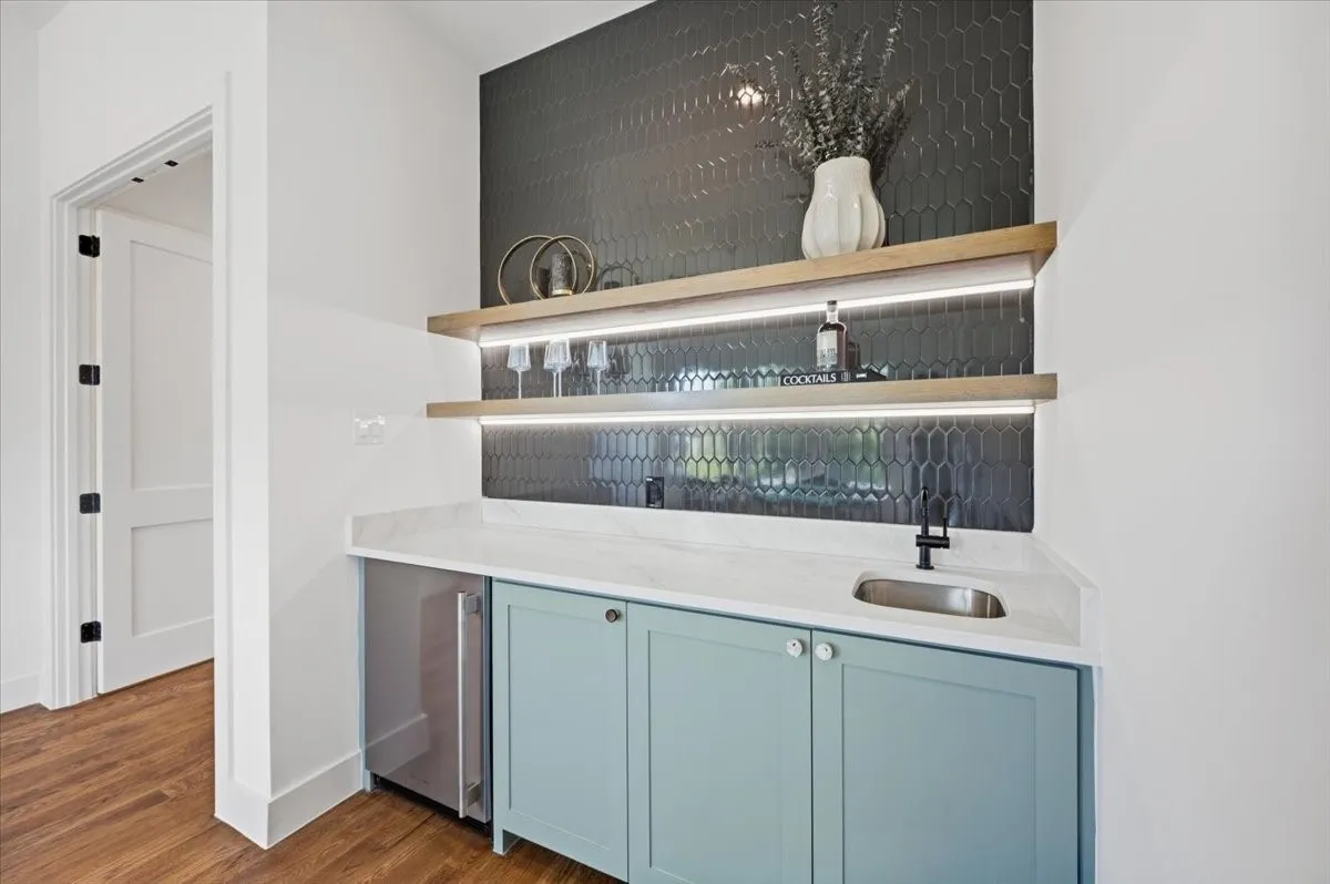 Built-in wet bar featuring a beverage refrigerator, light blue cabinetry, under-cabinet lighting, and a dark hexagonal tile backsplash