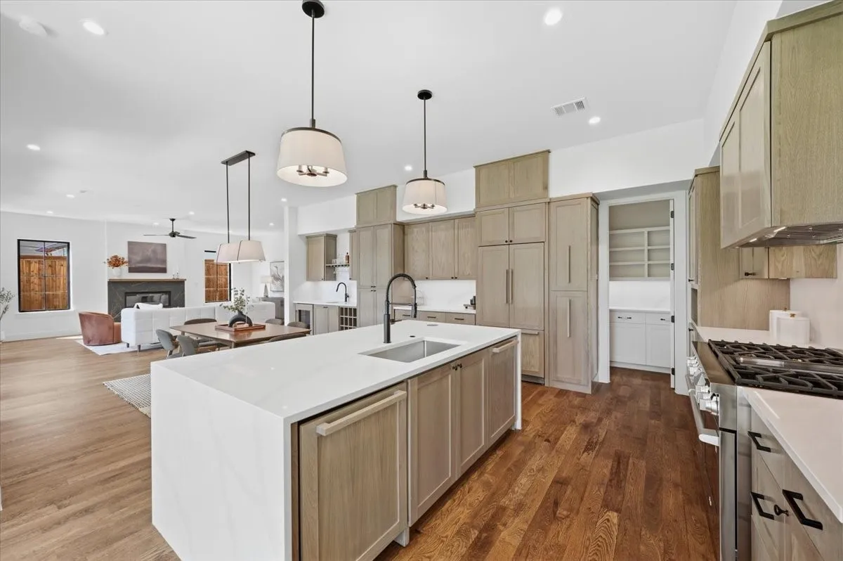 Gourmet kitchen featuring a large island, integrated appliances, natural wood cabinetry, a built-in pantry, and wood-finish flooring