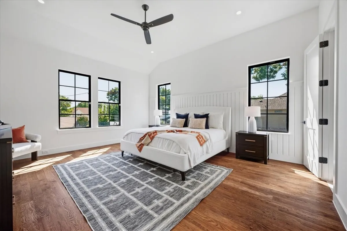 Vaulted ceiling with a black ceiling fan, dark wood-finish flooring, white walls, and black-framed windows