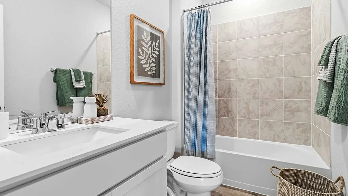 White vanity with an integrated sink and chrome faucet, large rectangular mirror, and a tiled shower-over-tub combination