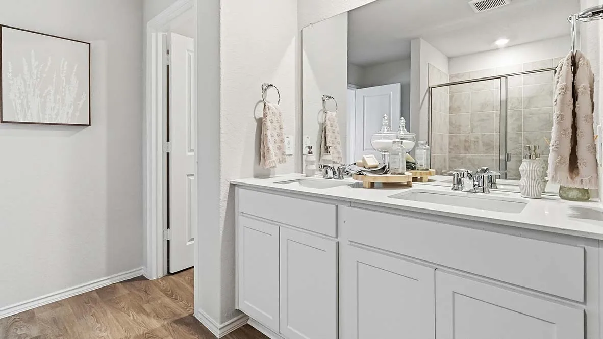 Dual undermount sinks with chrome fixtures, expansive vanity with white cabinetry, large vanity mirror, and wood-finish flooring