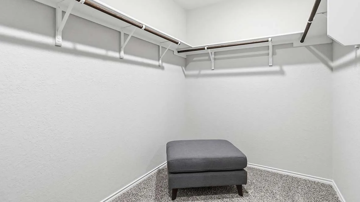 Built-in closet shelving and hanging rods with textured wall finishes and gray-toned carpet flooring