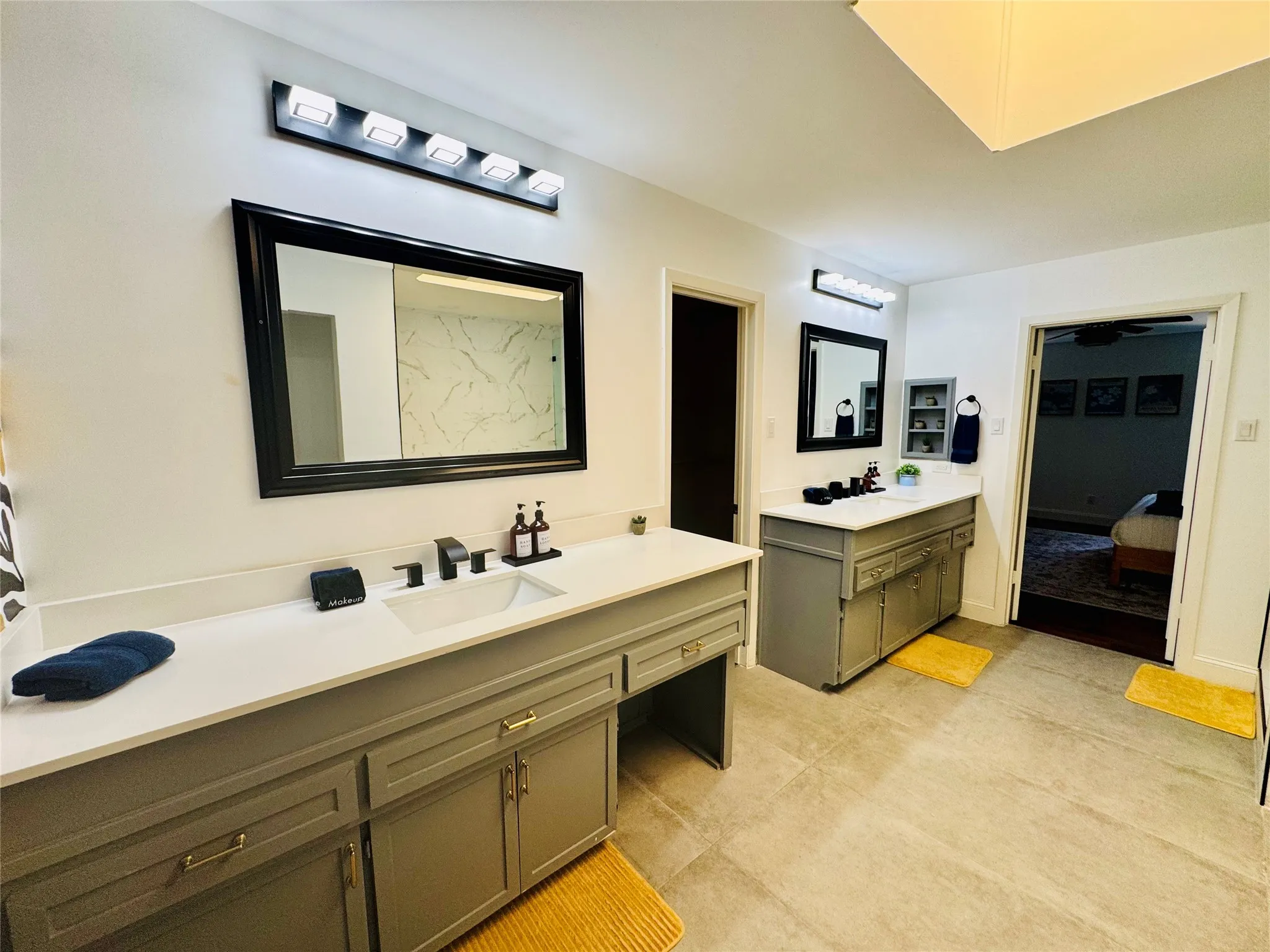 Expansive bathroom featuring dual vanities with integrated sinks, light countertops, and gray cabinetry with gold-tone hardware