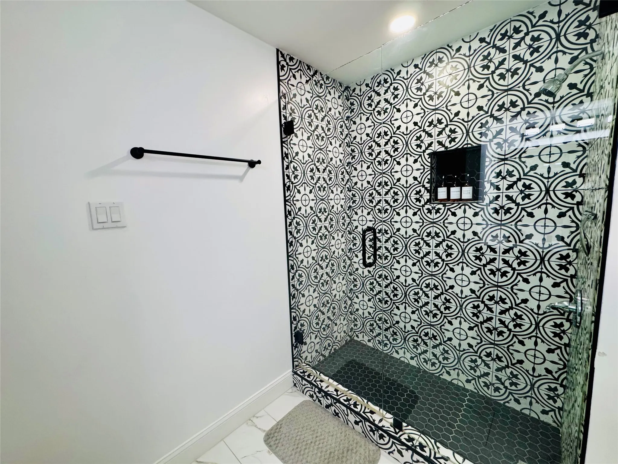 Walk-in shower with patterned wall tile, black hexagon floor tile, and a built-in shower niche