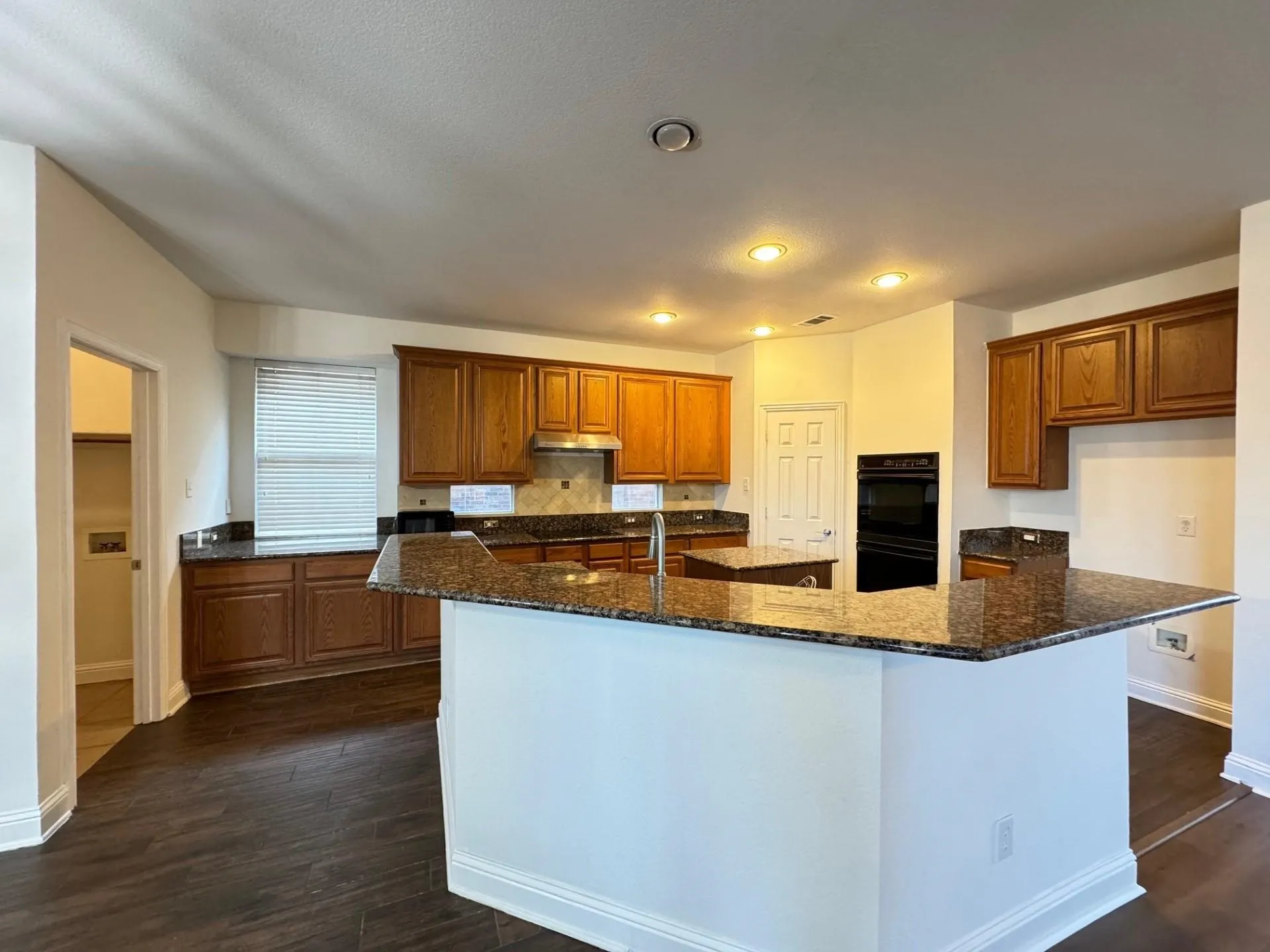 Kitchen featuring wood-finish flooring, recessed lighting, wood cabinetry, stone countertops, and built-in double ovens
