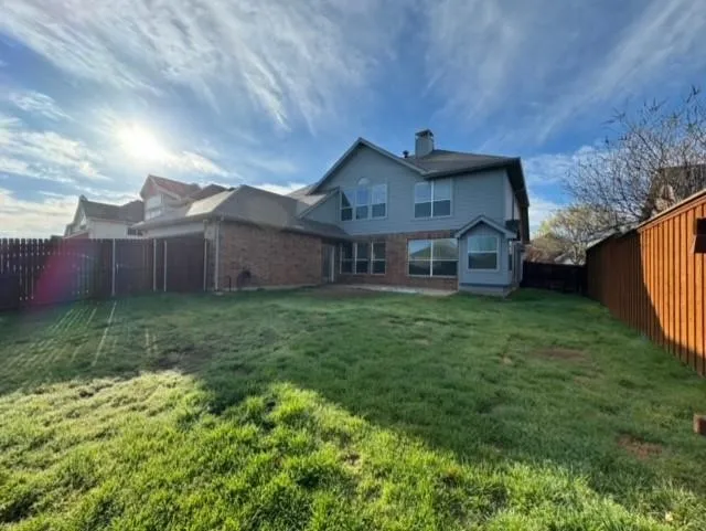 Expansive backyard with a manicured lawn, brick and siding exterior, multiple windows, and a privacy fence