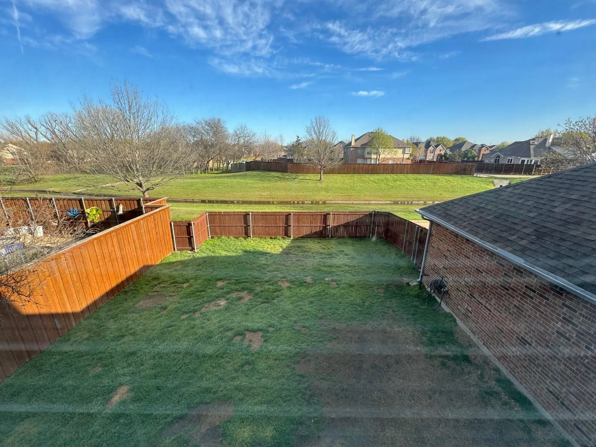 Expansive backyard featuring a manicured lawn, wood fencing, and a brick exterior