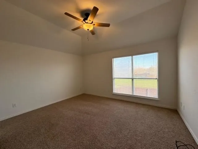 Vaulted ceiling with an attached ceiling fan, large window with blinds, and wall-to-wall carpeting