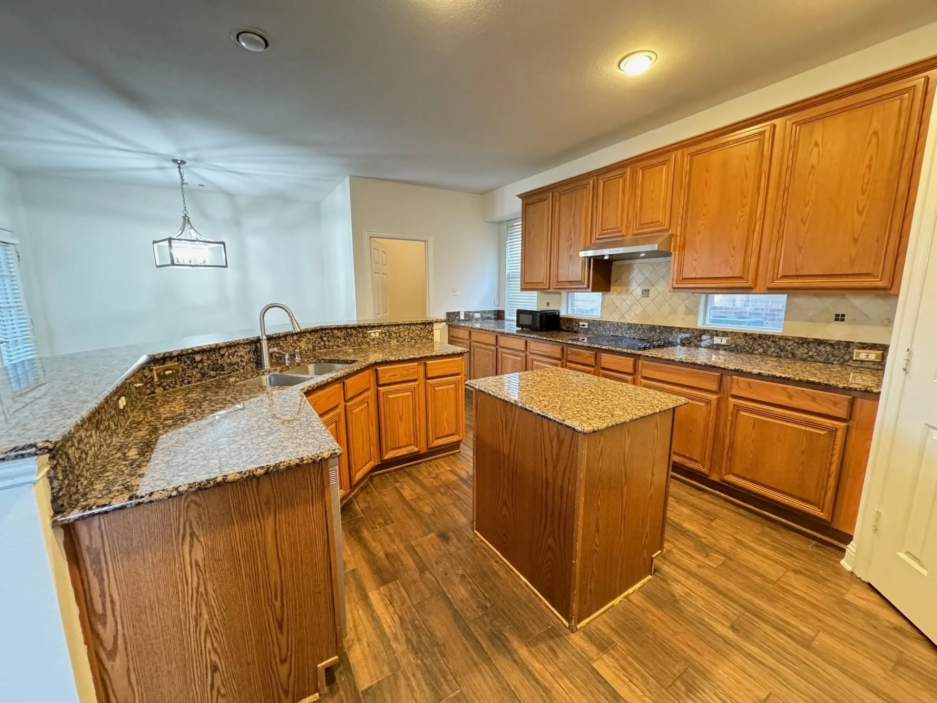 Kitchen featuring wood-finish flooring, wood cabinetry, stone countertops, a tile backsplash, and a central island
