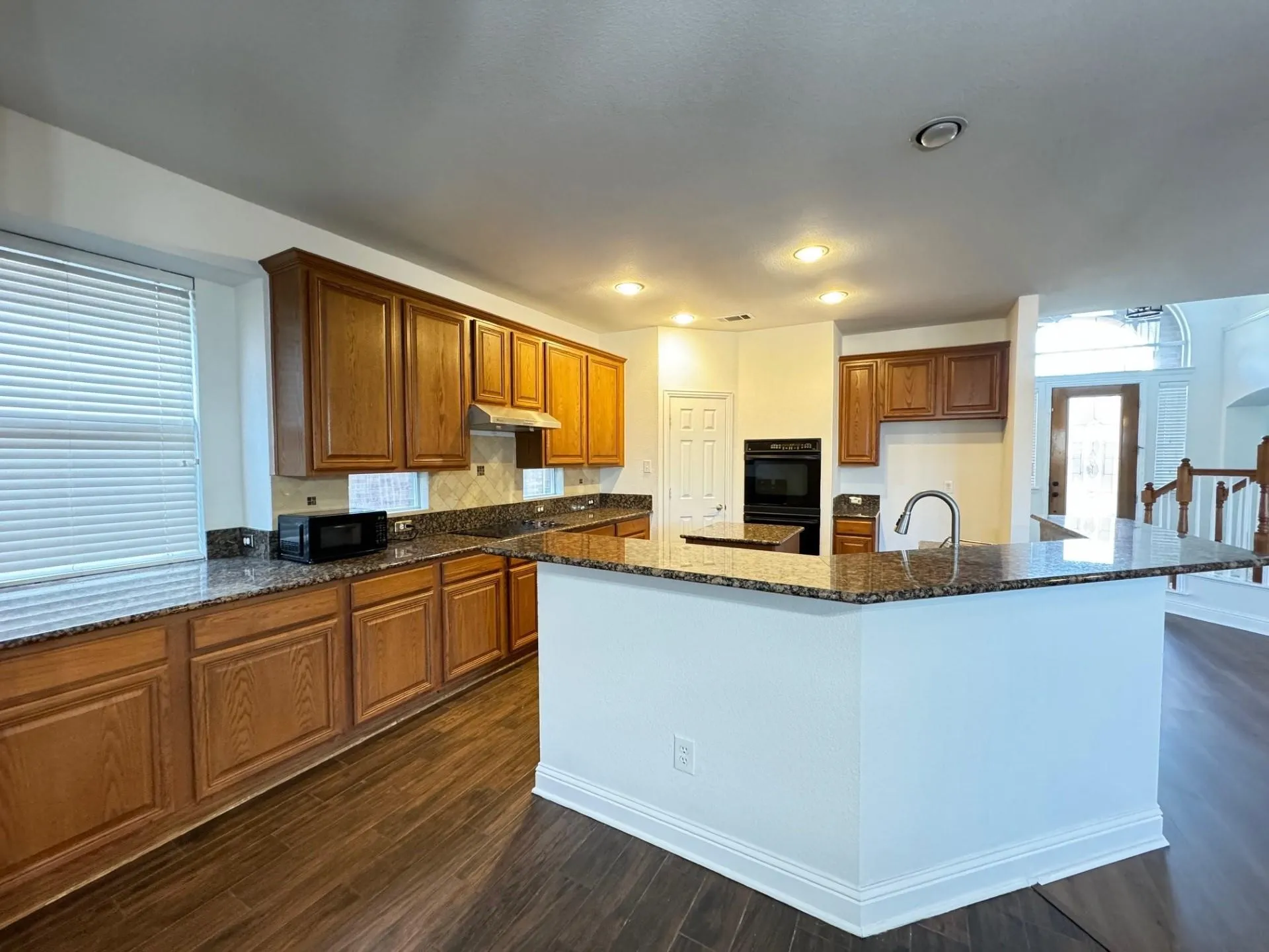 Kitchen featuring wood-finish flooring, recessed lighting, wood cabinetry, granite countertops, and a built-in oven