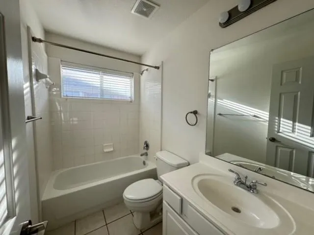 White tile flooring, white bathtub, white tiled shower surround, integrated sink with white countertop, and vanity mirror