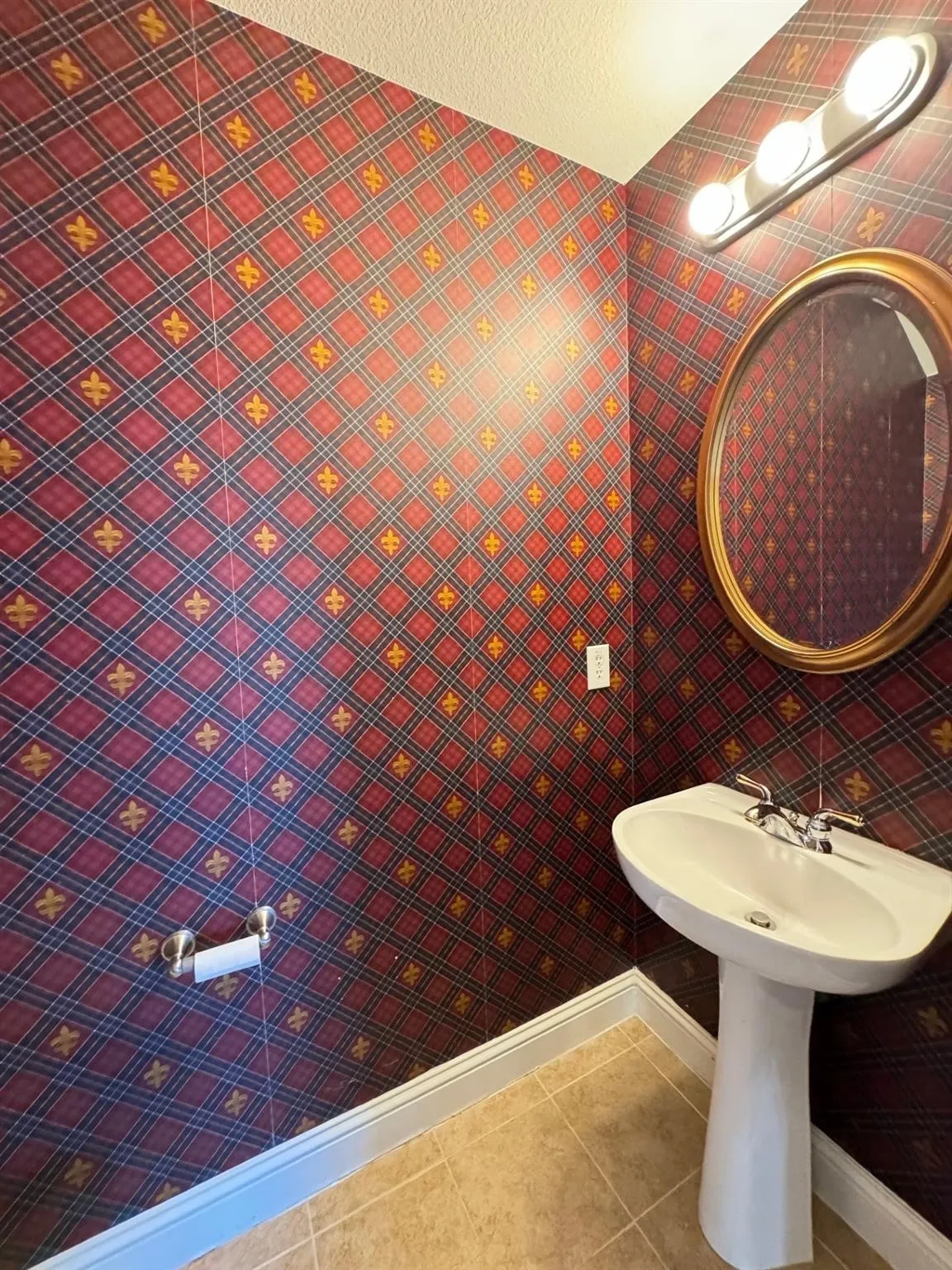 Pedestal sink with chrome faucet, oval framed mirror, and three-light vanity fixture