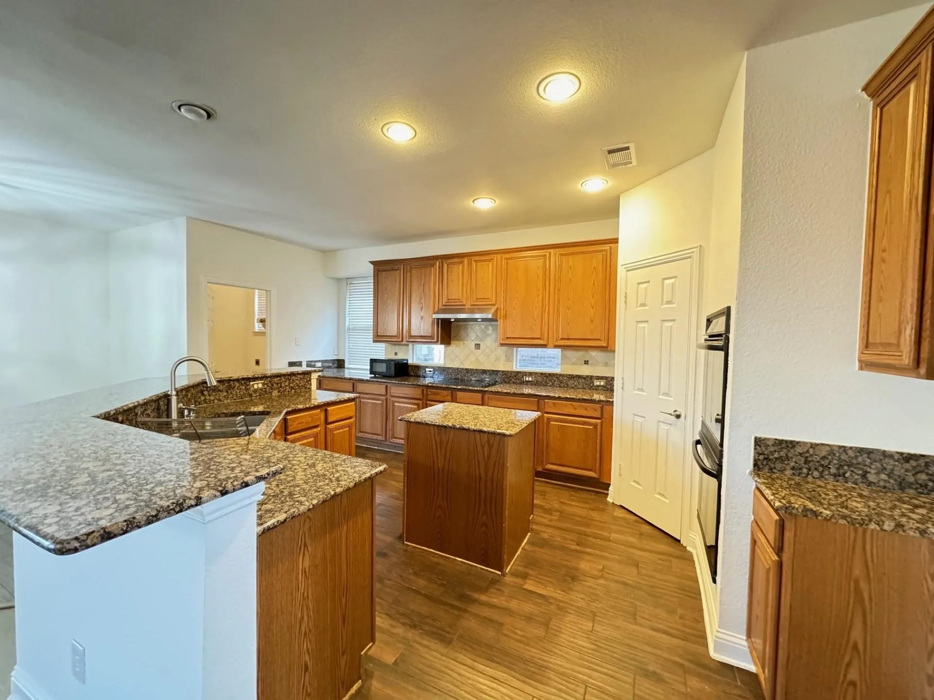 Kitchen featuring wood-finish flooring, granite countertops, wood cabinetry, a built-in oven, and recessed lighting