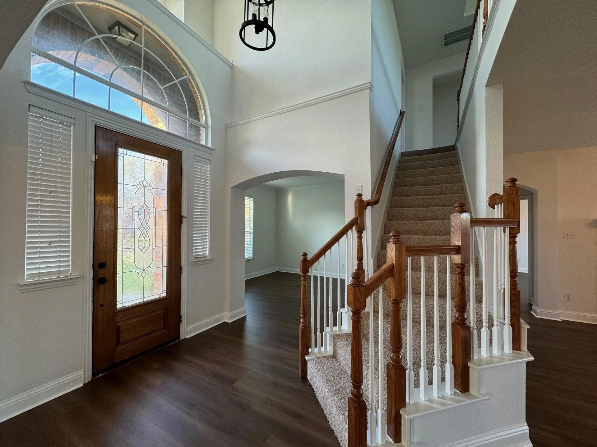 Two-story entryway featuring wood-finish flooring, a decorative glass front door, and a staircase with wood newel posts and white balusters