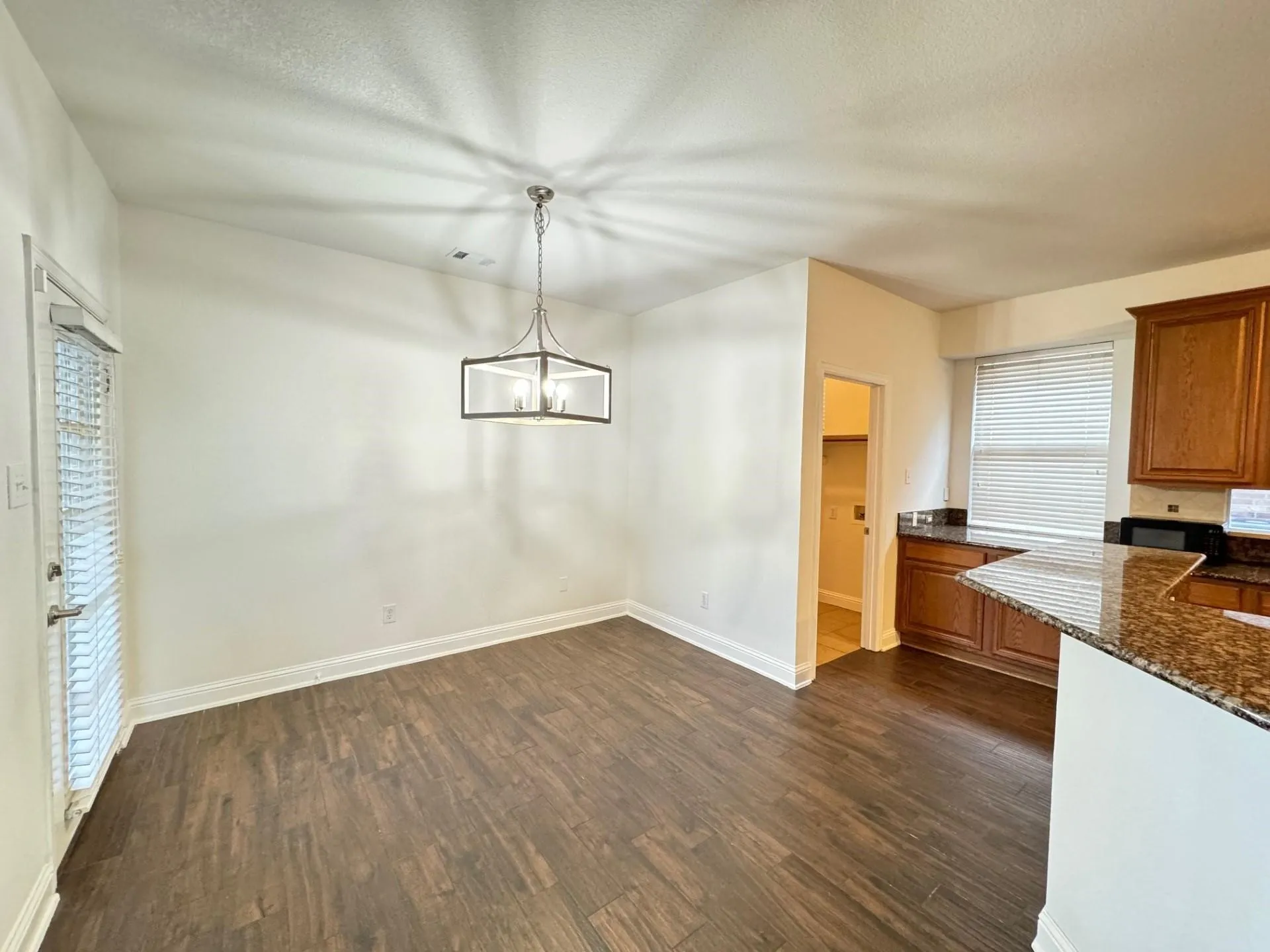 Wood-finish flooring, contemporary chandelier, white walls, and dark wood cabinetry with stone countertops